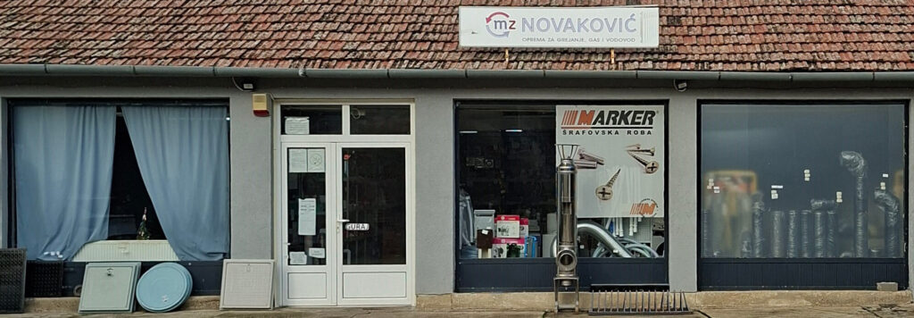 Glavni ulaz u prodavnicu M.Z. Novaković u Kikindi. Na izlogu je istaknuta reklama za Marker šrafovsku robu i vidljive su dimovodne cevi i oprema za grejanje, gas i vodovodne instalacije.